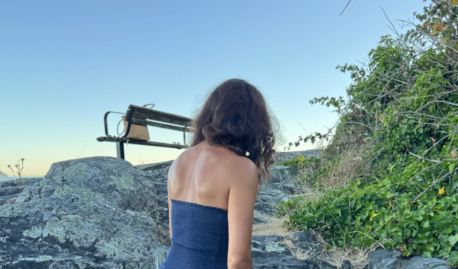 Woman standing on a rock with a bench and greenery in the background