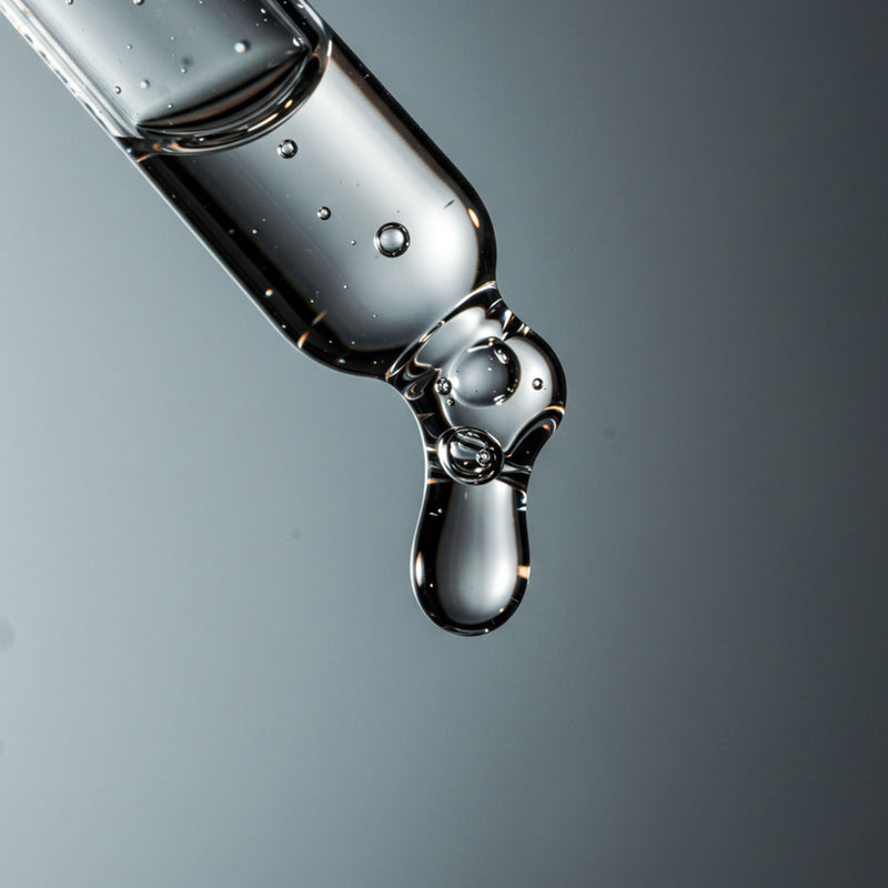 Close-up of a dropper with liquid dripping against a gray background
