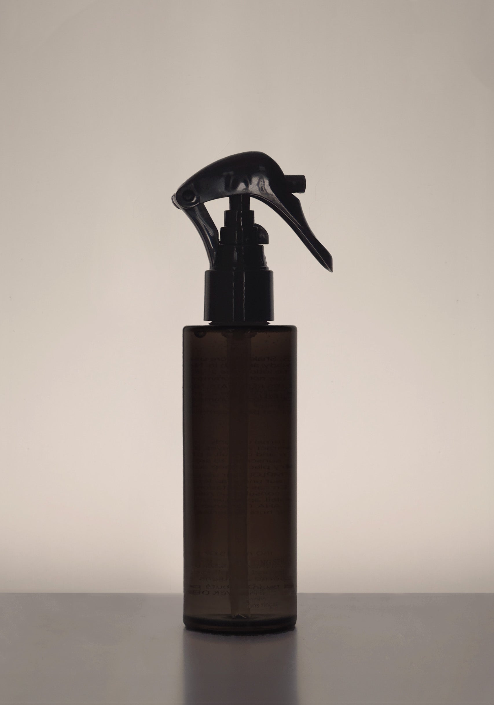 Shadowed dark brown spray bottle against neutral background